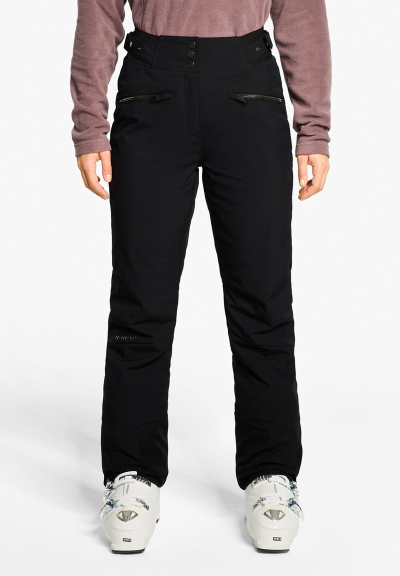 Person wearing black high-waist ski pants with zippered pockets, a mauve long-sleeve top, and white ski boots on a white background.