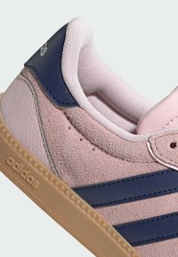 Baskets Adidas avec une tige en daim rose, des accents bleu marine et une semelle en caoutchouc texturée. Présente trois bandes bleu marine et un col rembourré.