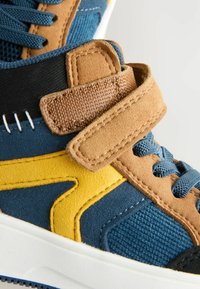 Sneaker aus einer Kombination von blauen Wildleder, braunen Akzenten, gelben Designdetails, einem Stoffriemen und strukturierten Paneelen. Verfügt über eine weiße Sohle.