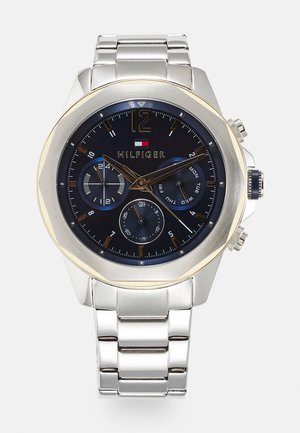 Montre en acier inoxydable avec un cadran bleu marine, une lunette en or et plusieurs sous-cadrans. Elle dispose d'un bracelet à maillons et de grands index numériques.