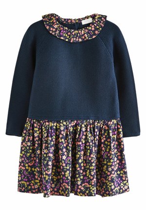 Granatowa sukienka z długimi rękawami i topem o teksturowanym dzianinowym wzorze. Spódnica w kwiatowy wzór z różowymi, żółtymi i fioletowymi kwiatami na ciemnym tle.