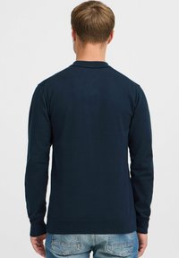 Polo �à manches longues bleu marine fabriqué en tissu doux et léger, avec un col et des poignets côtelés, vu de dos.