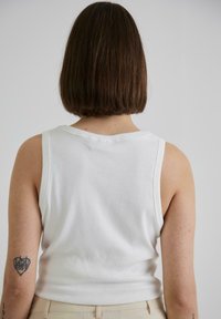 Hvid ribbet tanktop med et tætsiddende design, brede stropper og rund halsudskæring, set fra ryggen.