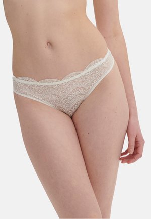 Kobieta w białej koronkowej bieliźnie z falistymi krawędziami, ukazana od talii do górnej części ud na jednolitym tle.