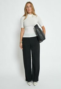 Top blanco de manga corta, pantalones de pierna ancha negros y tacones blancos puntiagudos. Modelo con un bolso negro con detalle de cremallera.