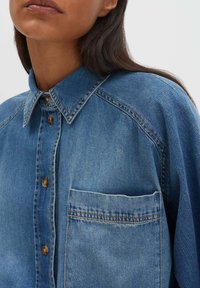 Jeanshemd in Hellblau mit spitzem Kragen, Brusttasche und durchgehender Knopfleiste. Verfügt über sichtbare Nähte und eine lockere Passform.