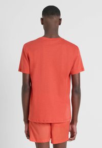 T-shirt kratkih rukava u koraljnoj boji s okruglim izrezom, glatke teksture i opuštenog fit-a, uparen s odgovarajućim kratkim hlačama.
