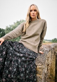 Brązowy sweter dzianinowy z okrągłym dekoltem, w zestawie z czarną, kwiatową spódnicą maxi z purpurowymi i szarymi akcentami. Teksturowany materiał, zwiewny fason.