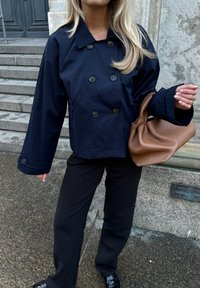 Jūras spēku dubultā jaciņa ar lieliem melniem pogām, valkāta ar melnajām biksēm. Brūna ādas plecu soma ar mīkstu, teksturētu apdari.