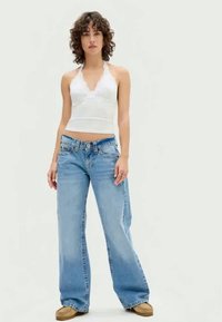 Hvit halterneck topp med en tettsittende livdel, parret med lyseblå baggy denimjeans. Myk tekstur, klassisk fem-lomme design og minimal maskinering.