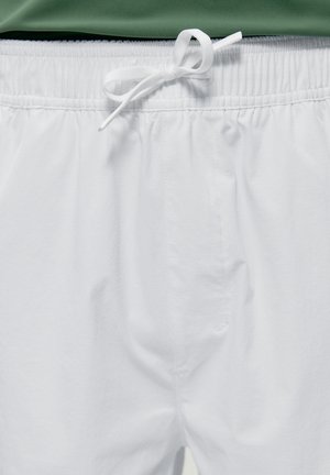Shorts con elastico bianco in vita e coulisse bianca annodata, indossati con un top verde parzialmente visibile sopra.