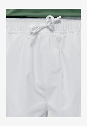 Weiße Shorts mit elastischem Bund und gebundenem weißem Kordelzug, kombiniert mit einem teilweise sichtbaren grünen Oberteil.