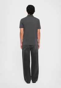 Dark gray polo shirt with short sleeves, made of soft fabric, paired with loose-fitting black jeans. Minimalist design with no patterns.