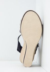 Sandale noire avec une semelle texturée, dotée d'une tige douce et tissée ainsi que d'un design à brides croisées. La semelle est de couleur claire et présente un motif.