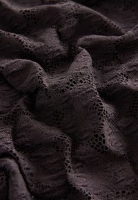 Tmavá krajka s propracovanými, jemnými vzory a strukturovaným povrchem, který vyzařuje jemnost a hloubku.