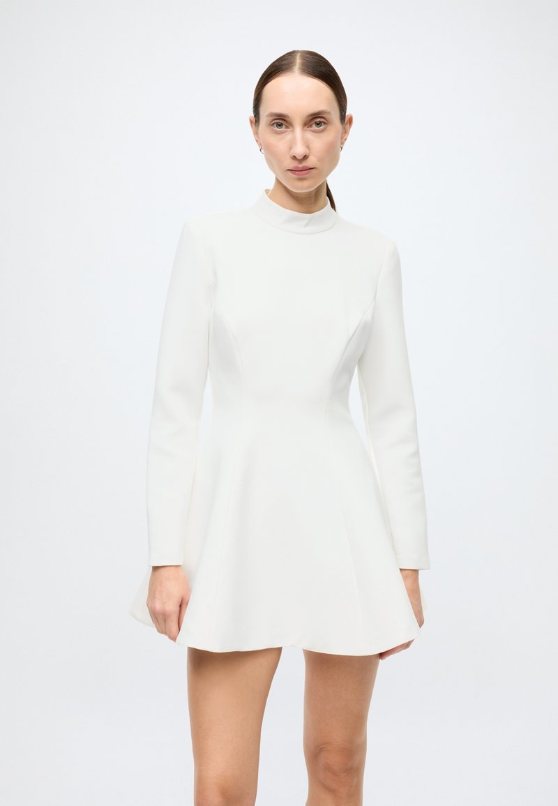 White long-sleeve dress with a fitted bodice, flared skirt, and high neckline, made of smooth fabric. Simple design with no visible patterns.
