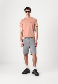 Lys rosa bomull t-skjorte, grå denimshorts, svarte sneakers med hvite sokker, og mørke solbriller. Uformelt antrekk med avslappet passform.