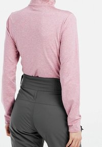 Långärmad rosa topp med hög hals, tillverkad av ett strukturerat tyg, kombinerad med högmidjade mörkgrå byxor med en slät yta.