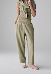 Top corto verde oliva abbinato a pantaloni jogger larghi verde oliva con vita elasticizzata. Tessuto morbido e dettagli di cuciture sottili.