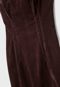 Robe en velours bordeaux à la coupe ajustée, avec des coutures latérales et une texture douce, mettant en valeur une couleur riche et profonde avec un éclat subtil.