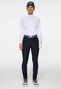 Vit långärmad sporttröja, marinblå tajta byxor, grått bälte, vita och blå sneakers, vit golfhandske, blå keps med logotyp.