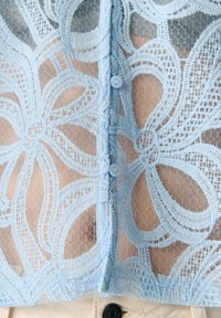 Light blue lace fabric with floral patterns and buttons, revealing skin underneath, paired with beige pants and a visible button.