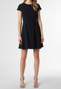 En kortärmad, mörkblå klänning med texturerad tyg, åtsittande liv och utställd kjol. Matchas med silverfärgade klackar med ankelskaft.