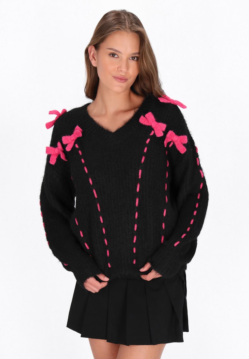 Schwarzer Pullover mit V-Ausschnitt, rosa Schleifendetails an den Schultern und kontrastierendem rosa Stich entlang der Vorderseite. Weicher, strukturierter Stoff.
