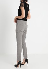 Czarna bluzka z koronkowymi rękawami i dziurką na plecach, zestawiona z szarymi, w kratę dopasowanymi spodniami i czarnymi szpilkami.