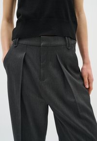 Pantalones grises con plisados, hechos de tejido texturizado con un ajuste a medida, que cuentan con trabillas para cinturón y bolsillos laterales.