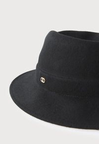 Cappello fedora nero in feltro con una larga visiera e un piccolo emblema decorativo dorato sulla fascia.