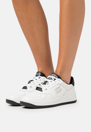 Zapatillas blancas con detalles y logo en negro. Parte superior de cuero suave, punta redonda, cierre de cordones y suela de goma texturizada.
