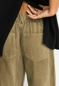 Khaki corduroy pants with a relaxed fit, featuring an elastic waistband, side pockets, and a vertical ribbed texture.