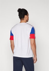 Camiseta de hombre de manga corta en blanco, azul y rojo. Presenta mangas en bloques de color y rayas laterales. Tejido suave con un corte relajado.