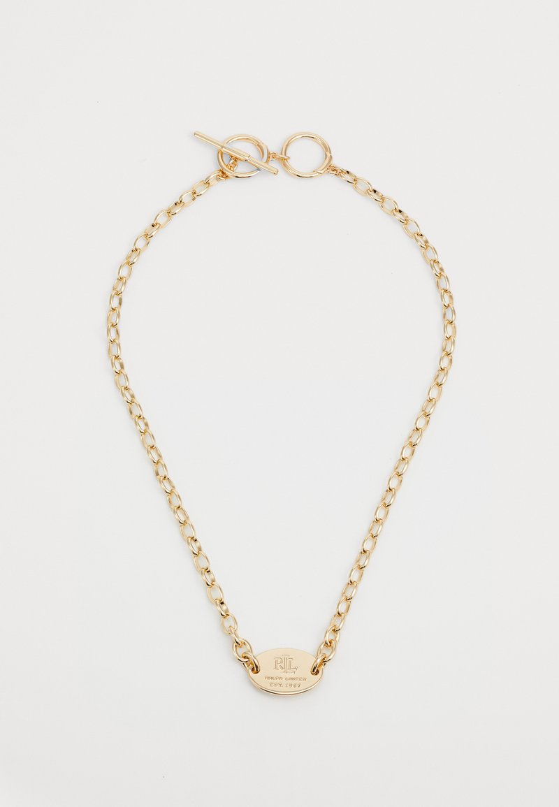 Colar de corrente dourada com fecho tipo toggle e um pendor oval apresentando um logótipo gravado e a data de fundação gravada na superfície.