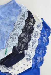 Cinq paires de sous-vêtements à dentelle en bleu, blanc, noir et tissus à motifs, disposées en chevauchement sur une surface claire.