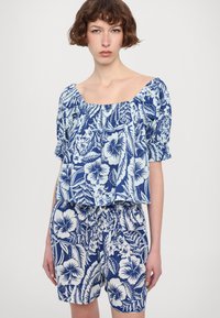 Blå blomstertrykt topp med puffede ermer og av- skuldret halslinje, kombinert med matchende shorts med lignende design og elastisk midje.