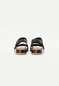 Black leather sandals with multiple strap design, flat sole, and tan accents. Reinforced heel and simple, minimalist construction.
