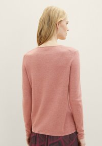 Langarmtrui van zacht roze breimateriaal, met een ronde halslijn en subtiele naaddetails, gecombineerd met een patroonskirt.