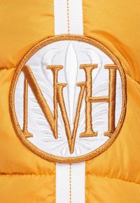 Gul pufferjakke sektion med et rundt broderet logo med "NVH", omgivet af hvidt med gyldne detaljer og en lodret hvid stribe.