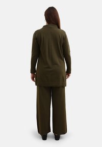 Olijfgroene twee-delige outfit met een blouse met lange mouwen en kraag, en een wijde broek. Materiaal heeft een gladde textuur en een comfortabele pasvorm.
