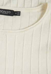 Cremfarbener gerippter Pullover mit Rundhalsausschnitt, aus weichem Strickmaterial. Das Etikett zeigt die Marke "SOAKED" und die Größe "M".