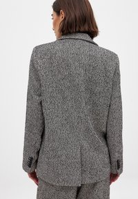 Sakó s houndstooth vzorom v čiernej a bielej farbe, s klopovým golierom, jedným zadným rozventom a gombíkovými manžetami. Texturovaná tkanina.