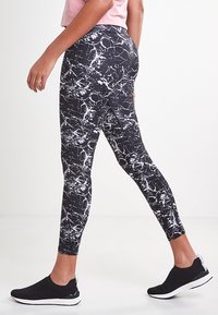Leggings noirs avec un motif marbré blanc, fabriqués dans un matériau extensible. Le design présente une coupe ajustée et une texture lisse.