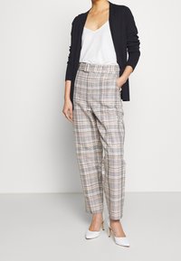 Beige rutiga högmidjade byxor med bälte, i kombination med en vit linne och svart kofta. Strukturerat tyg, skräddarsydd passform. Vita klackar.