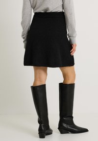 Jupe en tricot noire avec un design évasé et une finition texturée, associée à des bottes noires montantes élégantes avec un bout pointu et un talon bloc.