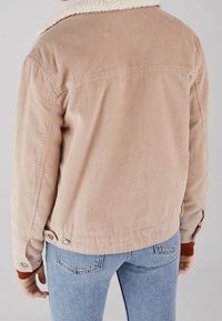 Giacca in corduroy di un beige chiaro con un colletto di piuma crema, caratterizzata da righe verticali, tasche e dettagli con bottoni ai polsini e all'orlo.