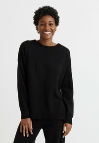 Maglione nero realizzato in materiale morbido. Presenta una vestibilità comoda, scollo rotondo e orlo a coste. Design semplice con un dettaglio di cucitura centrale.