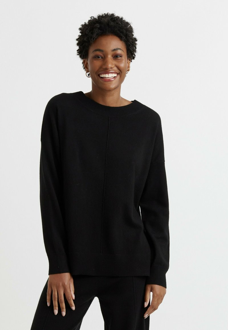 Maglione nero realizzato in materiale morbido. Presenta una vestibilità comoda, scollo rotondo e orlo a coste. Design semplice con un dettaglio di cucitura centrale.