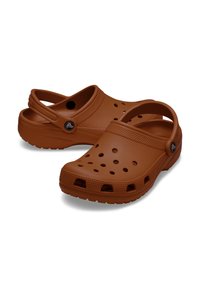Sabots en plastique marron avec une partie supérieure perforée, une bride au talon, une semelle texturée et un accent de logo. Comprend une forme arrondie pour le confort.